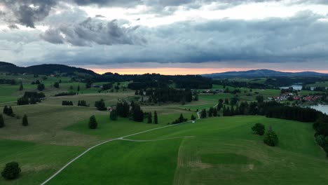 Sunset-glow-over-green-meadows-next-to-a-lake-at-a-cloudy-evening-in-summer