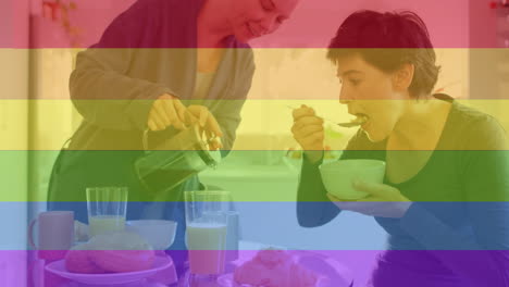 Animación-De-Las-Rayas-Del-Arco-Iris-Del-Orgullo-Sobre-Una-Feliz-Pareja-De-Lesbianas-Caucásicas-Tomando-Café-Y-Desayunando