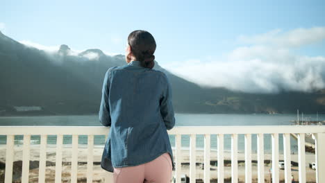 Woman enjoying ocean view from balcony, wearing denim jacket and leggings, copy space