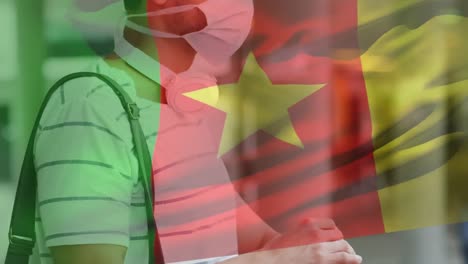 Animation-of-flag-of-cameroon-waving-over-latin-man-wearing-face-mask-in-city-street