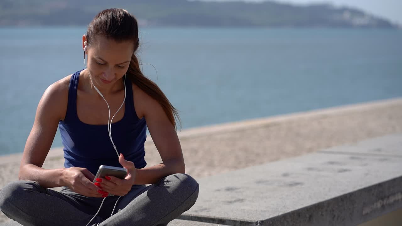mujer joven sonriente con auriculares usando teléfono celular en la orilla del río