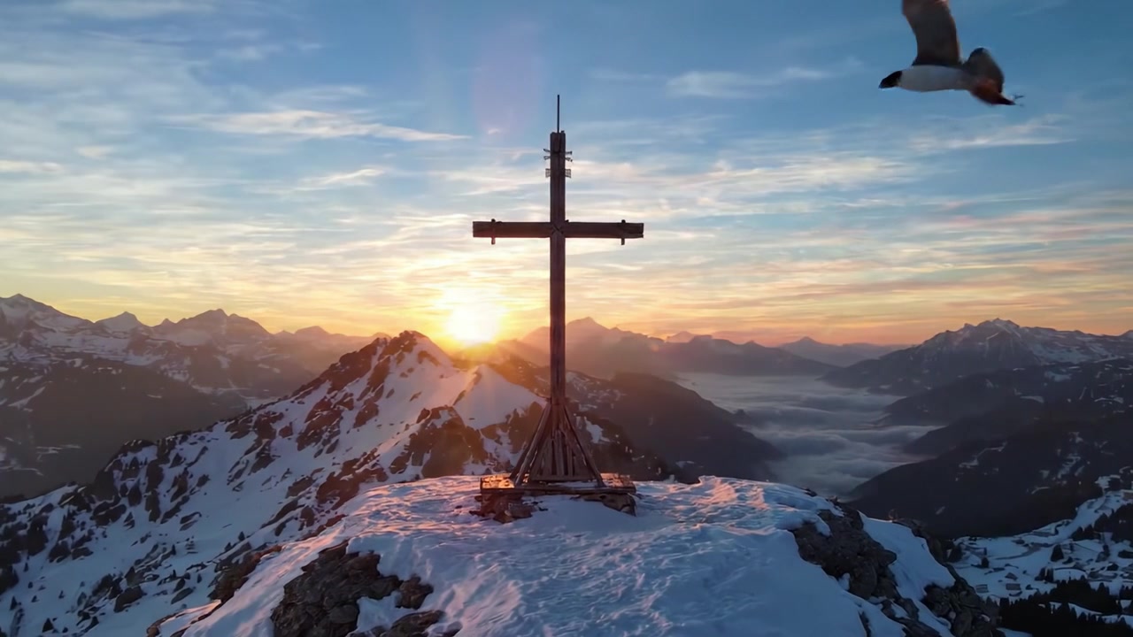 Eine atemberaubende Berglandschaft im Morgengrauen, die ein markantes Kreuz zeigt, das sich vor den goldenen Sonnenstrahlen und den majestätischen Gipfeln der Alpen im Hintergrund abzeichnet.