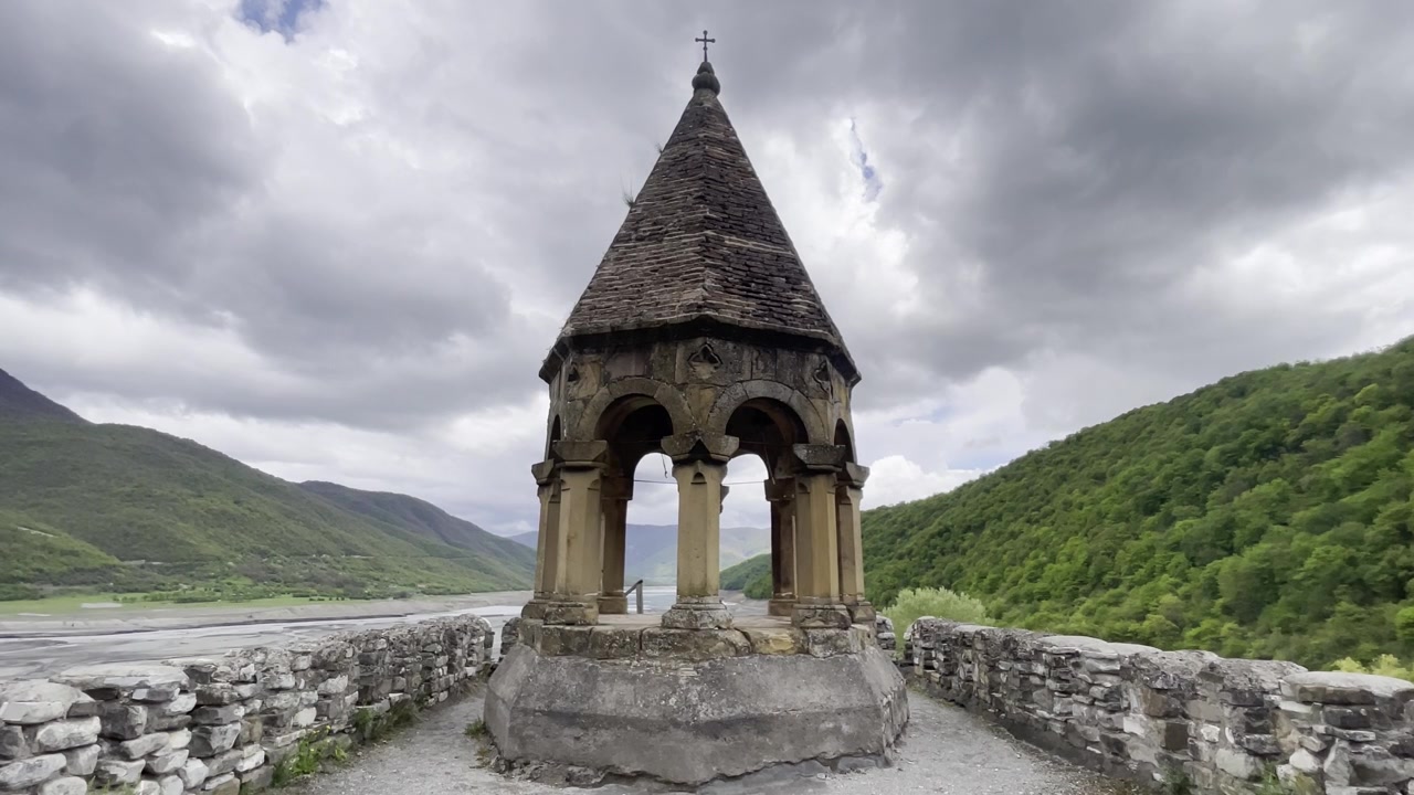 Nærbillede af det middelalderlige stenklokketårn ved Ananuri-fæstningen, Georgien. Traditionel georgisk-ortodoks arkitektur med et kegleformet tag, der overser de grønne bjerge og Zhinvali-reservoiret