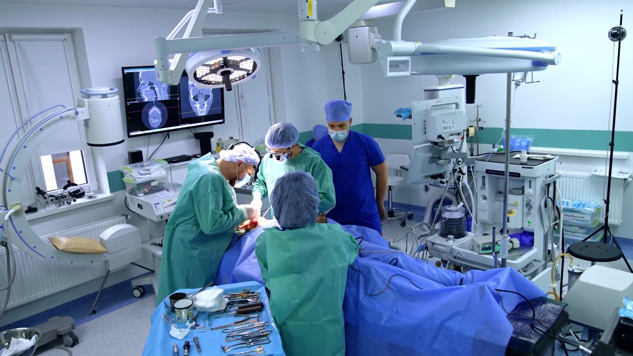 Maxillofacial surgery performed in modern operating room. Two male surgeons carry out operation assisted by female nurse. High angle view.