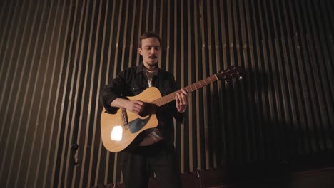 a handsome guy plays an acoustic guitar in an abandoned cinema. the musician sings a song and accompanies on the guitar