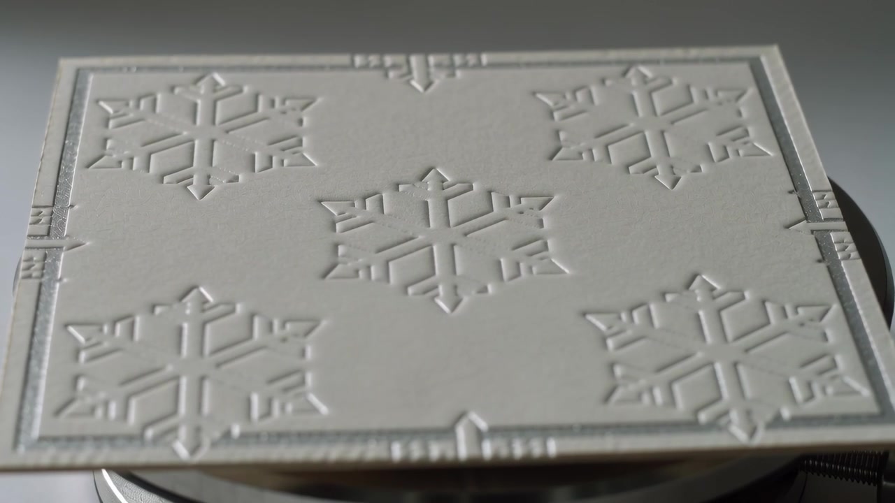 Rotating turntable carrying cardstock on tabletop revealing embossed snowflake, showing texture