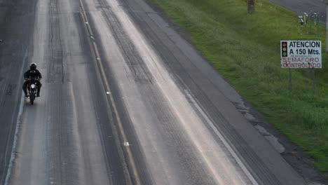 una motocicleta se acerca a la cámara por una ruta maltrecha evitando las huellas del uso frecuente de camiones pesados.