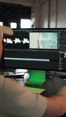 vertical - male sit near computer screen and use video editing software