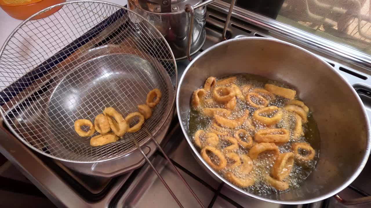 Anelli di calamari marocchini croccanti vengono fritti in olio bollente e ricoperti di pastella aromatizzata durante la preparazione tradizionale di frutti di mare. Una schiumarola solleva gli anelli appena cotti dall'olio caldo mentre ad