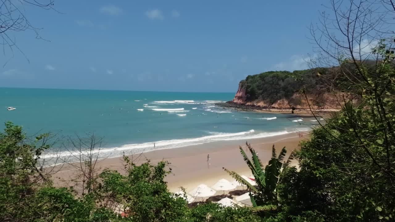 Ripresa in tilt up che rivela la splendida e famosa destinazione turistica tropicale, la spiaggia di Madeiro a Pipa, Brasile, nello stato di Rio Grande do Norte, circondata da scogliere con piccole onde perfette per il surf.