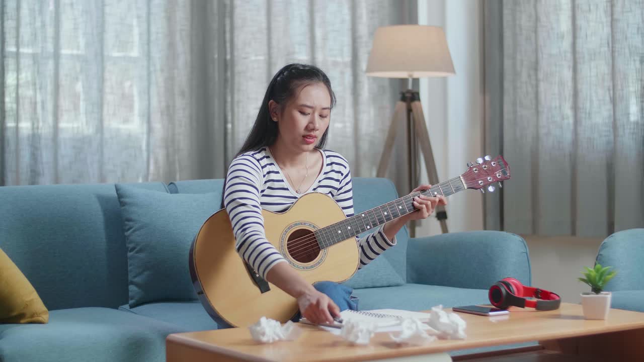 기타를 연주하면서 노래 가사를 쓰기 위해 고군분투하는 여성