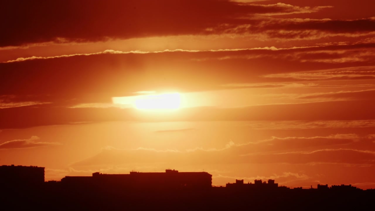 Golden sunset descending behind a dense urban skyline, silhouetting mid-rise residential buildings