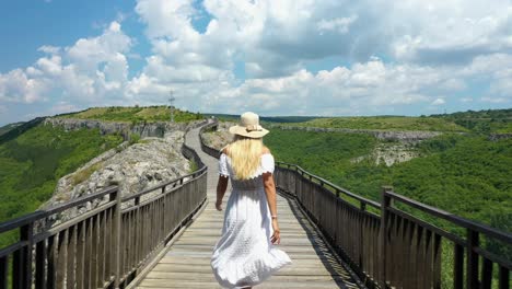 woman in white dress and a sun hat opens gate doors, walks on bridge