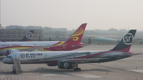 during dusk at beijing international airport, china, airplanes from hainan airlines, a prominent chinese airline, and sf express, a global delivery and logistics company, are parked on the runway.