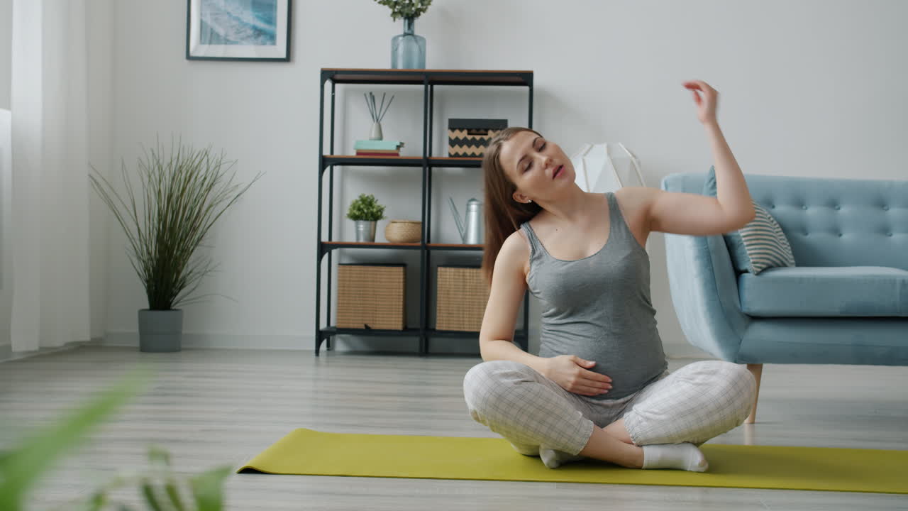 임신 한 여자 가 집 에서 스트레칭 하고 있다