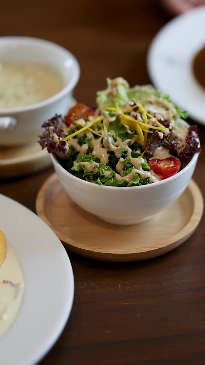 Close-up of hand arranging salad, soup, and omelette meal on wooden cafe table