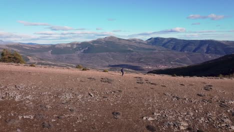 Aerial-shot-back-view-of-young-hiker-in-mountain-range-close-to-Madrid-during-afternoon-with-blue-sky-and-white-clouds