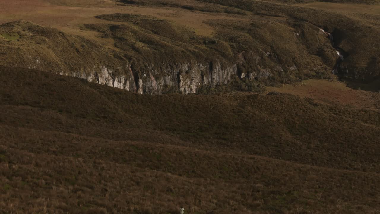 una mujer mirando el volcán chimborazo en ecuador, rodeado de un vasto terreno montañoso, desciende inclinado hacia arriba