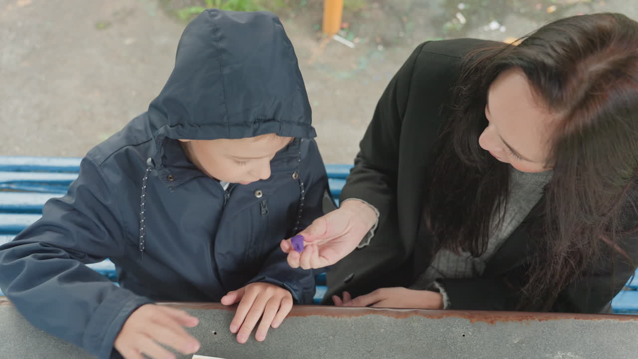 Konselor Asia membantu anak menyiapkan ransel, bimbingan yang tenang dan suportif dengan tangan memperbaiki gesper dan ritsleting, ransel biru dan jaket di bangku taman, transisi ke hari sekolah, membangun kepercayaan diri