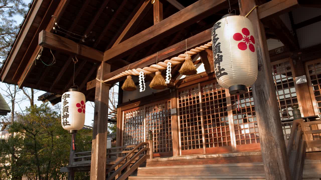 Low angle shot of wooden Shinto shrine building with paper lanterns and shimenawa rope