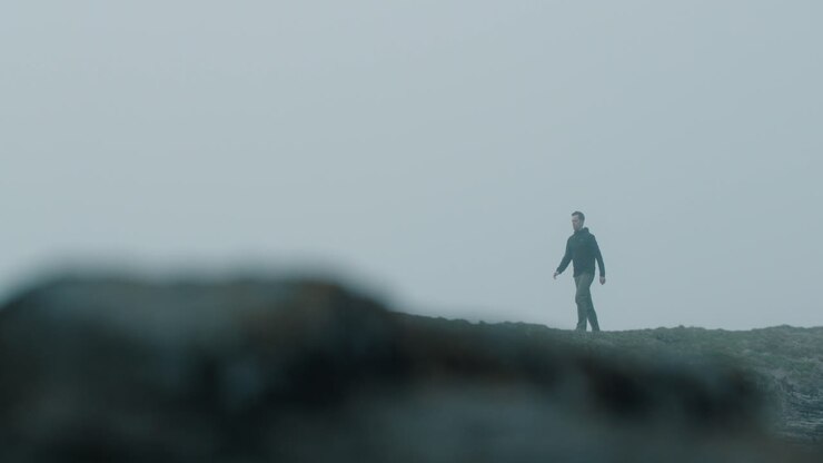 Man walking near cliffs on a foggy day in slow motion