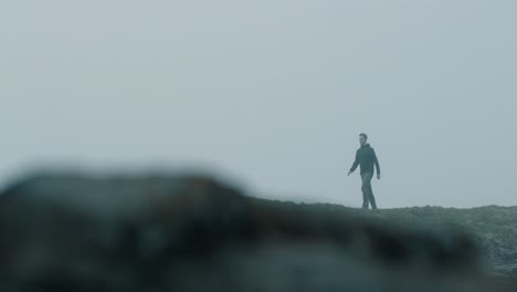 man walking near cliffs on a foggy day in slow motion