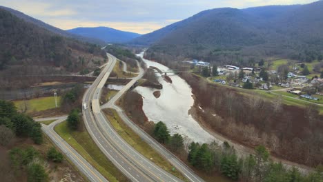 Flying-sideways-over-a-river-valley,-bridges,-a-highway,-and-small-town-with-very-little-traffic-in-small-town-america-during-late-fall