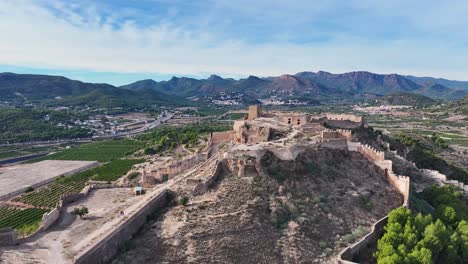 Filmischer-Flug-Mit-Einem-DRO-über-Dem-Höchsten-Teil-Der-Burg-Von-Sagunto,-Bei-Dem-Man-Die-Besucher-Beobachtet,-Mit-Einem-Wunderschönen-Hintergrund-Aus-Bergen,-Einem-Blauen-Himmel-Und-Weißen-Wolken,-Gefilmt-In-70-Mm-In-Spanien