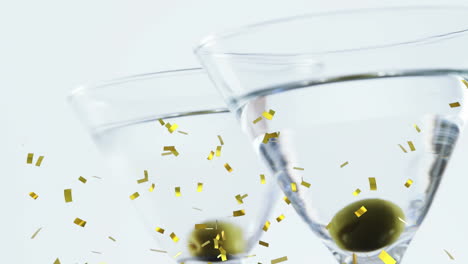 golden confetti falling over close up of olives in two cocktail glasses against grey background