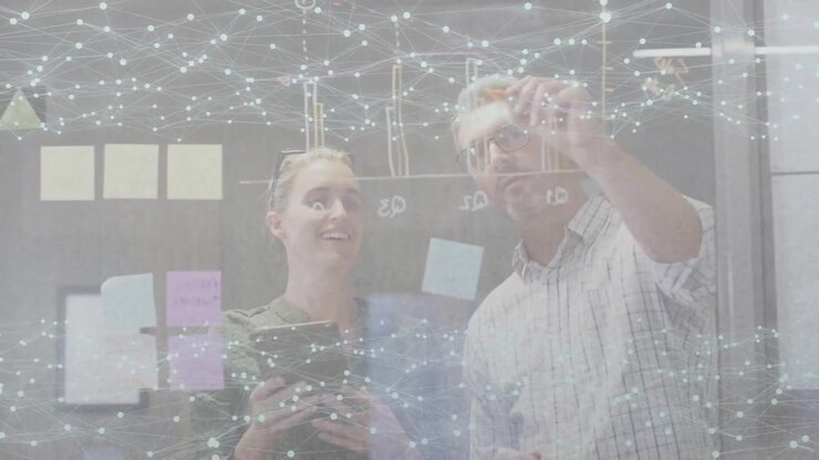 Woman placing sticky note on glass, partner marking diagram, finalizing business plan under overlay