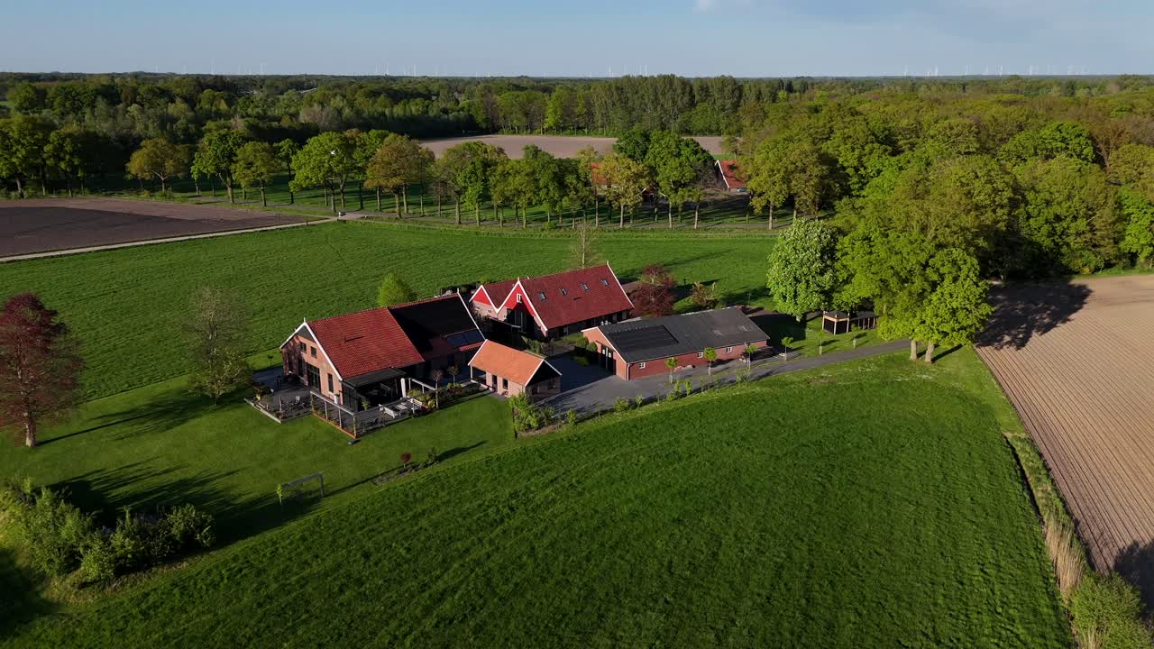 Well-kept farmers house with modern solar panels on roof. Golden sunset in quiet rural american neighborhood. Aerial orbit shot. Colored trees in forest landscape. Grass in garden of property.