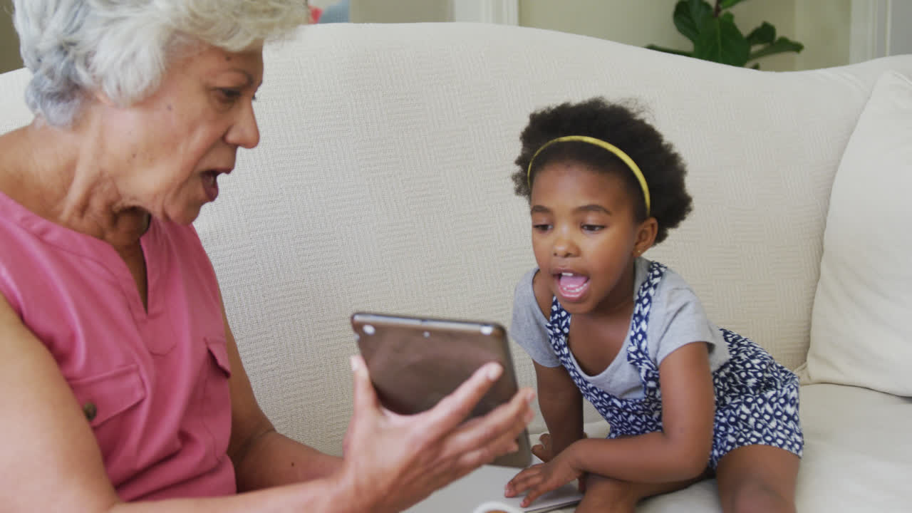 Happy african american grandmother with granddaughter using tablet in living room