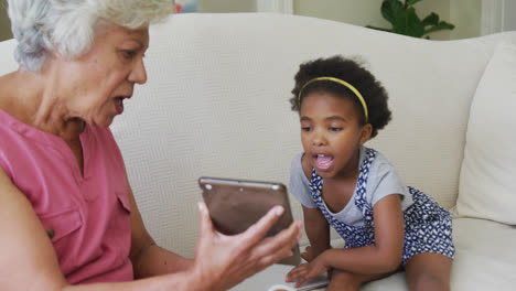 happy african american grandmother with granddaughter using tablet in living room