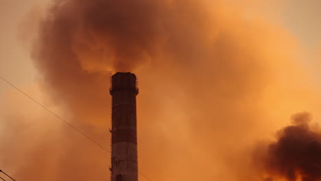 thick fumes from industrial chimneys smoking. clouds of dirty emissions pollute the atmosphere. puffs of smoke on the evening sky. polluting factory at sunset.