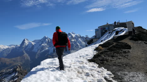 Hombre-Con-Abrigo-Rojo-Y-Gorra-Verde-Disfruta-De-Las-Maravillosas-Vistas-Y-Montañas-De-Jungfraujoch,-Conocido-Como-La-Cima-De-Europa