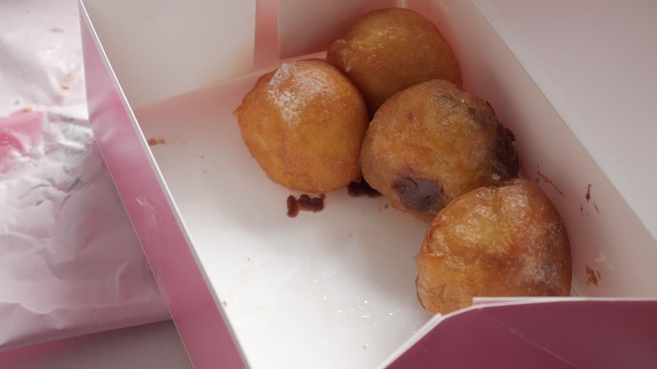 Buñuelos de viento, traditional spanish fritter, in pink box opened by male hand. Sweet from Spain served for All Saint's Day. Fried dough balls with different fillings: chocolate cream, etc.