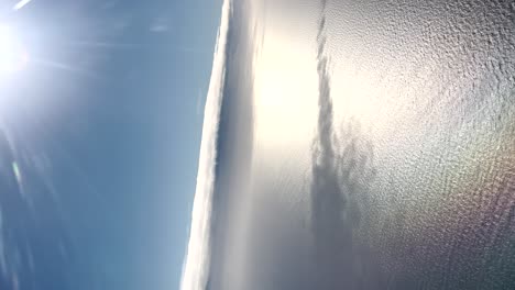 Vertical-aerial-view-of-the-blue-sky-and-sea-on-a-clear-day,-with-bright-sunshine-and-gentle-water-ripples