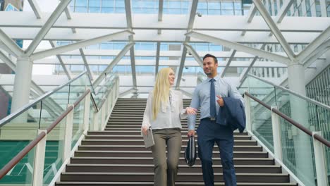 two happy office colleagues having fun conversation while walking down a flight of stairs outside office building - slow motion low angle dolly back