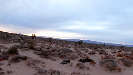 an abandoned and burned out car on along a trail in the mojave desert wilderness - aerial orbit view