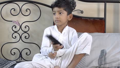 cute indian asian caucasian boy child changing tv channel with remote and trying to make it work by hitting it front view