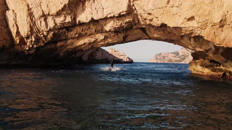 Drone-shot-of-someone-riding-an-electric-surfboard-through-Ibiza's-beautiful-waters-in-Spain