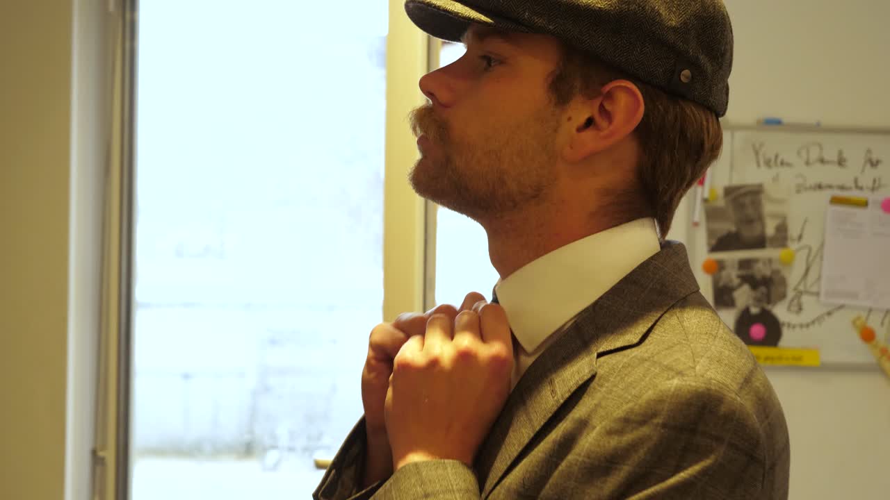 콧수염과 베레모가 있는 똑똑하고 멋진 남자가 대기실에서 자신과 넥타이를 준비하고 있습니다.