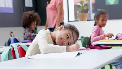 in school, girl smiling while writing in notebook at classroom desk