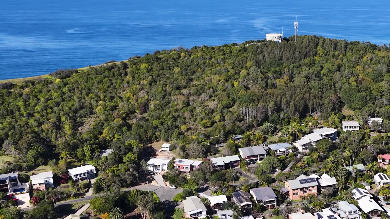 Korkealta kuvattu dronekuva esikaupunkitaloista, jotka sijaitsevat vihreässä metsässä meren rannalla Australiassa.