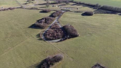 Aerial view of a winding rural road cutting through expansive grassy fields and scattered tree clusters near Wiltshire Downs in England, offering a peaceful and scenic countryside landscape