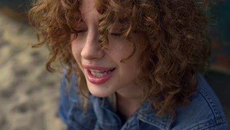 Playful-woman-blowing-curls-from-face-sitting-beach-near-old-boat-close-up.