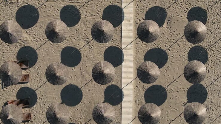 Woven beach parasols and boardwalk on hot sand form repeating pattern