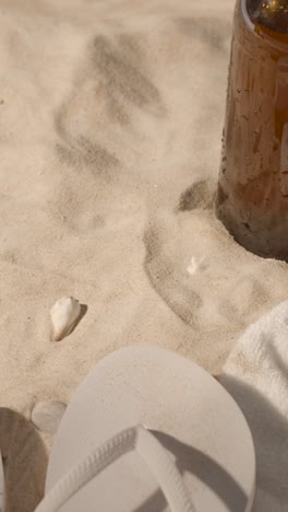 video vertikales sommerferienkonzept von sonnenbrillen, sonnenhut, flip-flops und kaltem bier am strand, handtuch auf dem sand