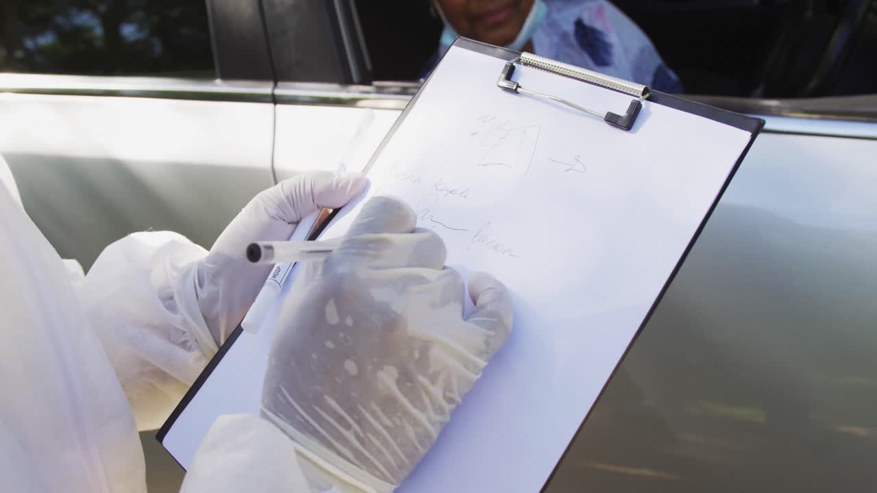 sección media de un trabajador de la salud con ropa de protección tomando notas en el clipboard en la carretera