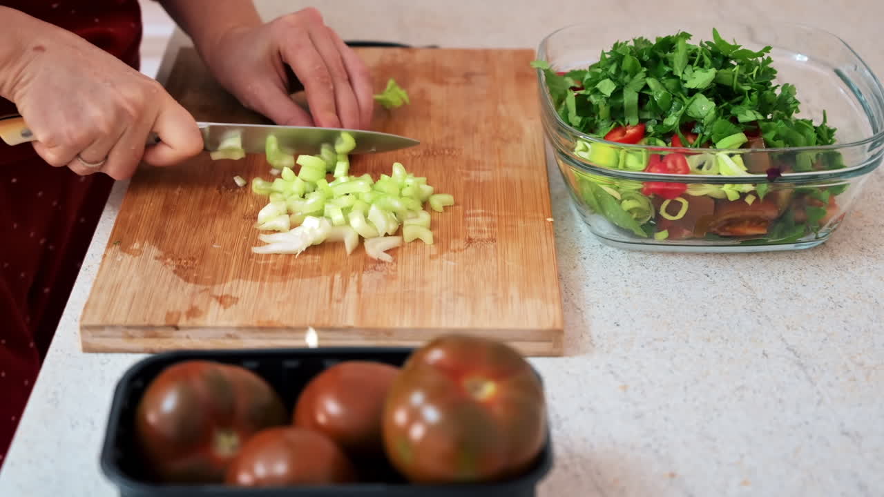 Woman slicing celery for a salad. Other ingredients in the dish next to it